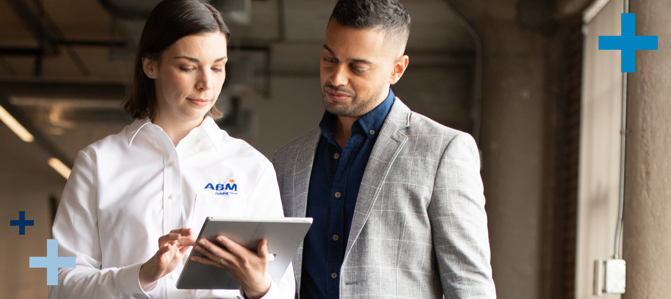 Woman in an ABM shirt sharing information on a tablet with a man in a suit jacket.
