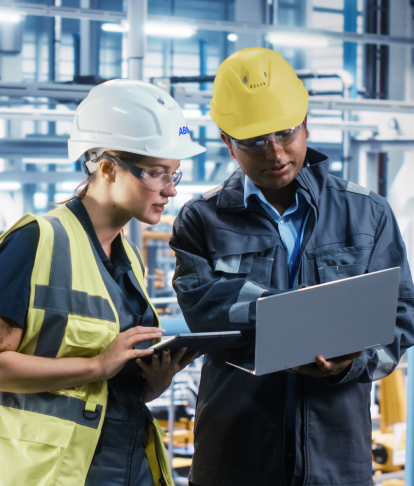 Two people in hardhats talking in a auto plant