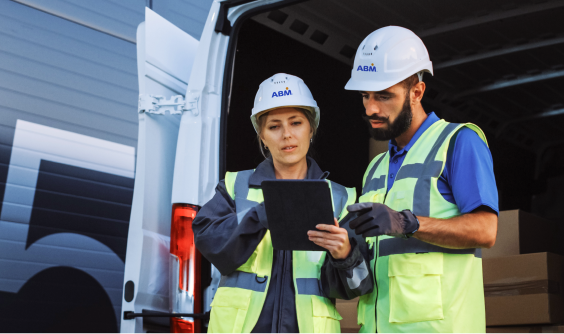 Two people in hard hats looking at an iPad behind a truck