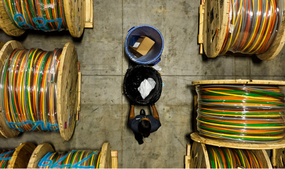 An overhead shot of a person pushing walking through a warehouse with  giant spools of wire