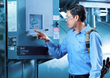 Male ABM engineer wearing a blue shirt pushing buttons on a large chiller machine