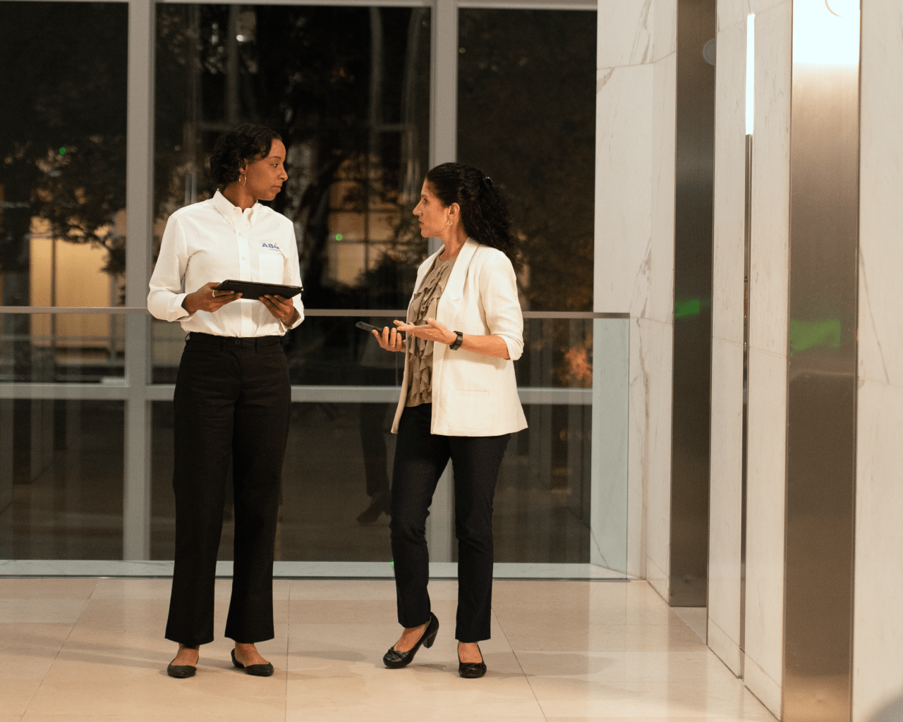 Female ABM engineer speaking with a hotel property manager beside the lobby elevators.